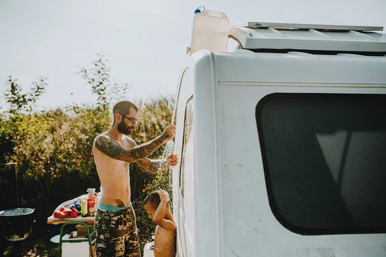 Man with Tattoos Giving Shower to His Son in front of the Caravan